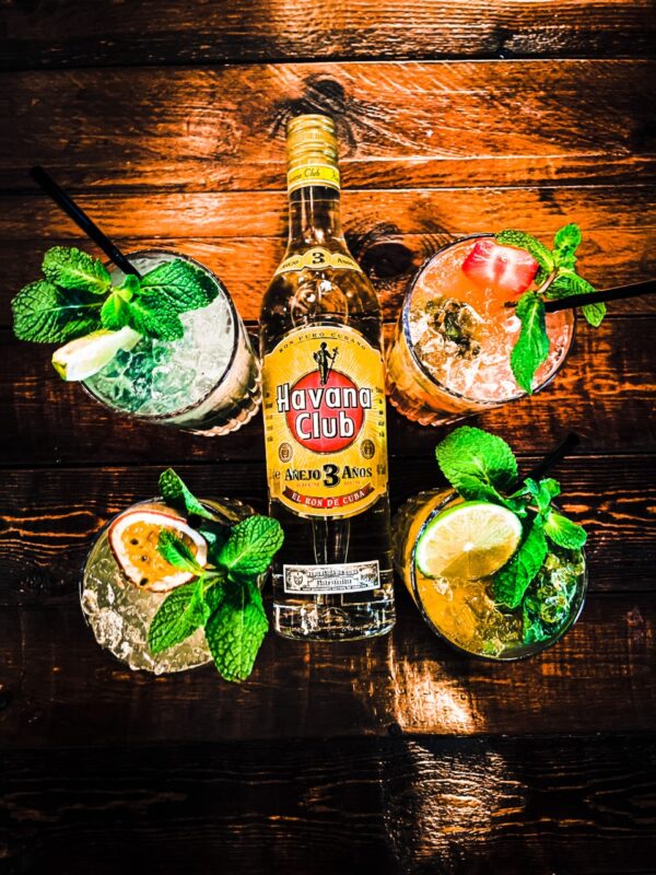 a bottle of Havana club on a wooden table with 4 glasses of mojito cocktails.