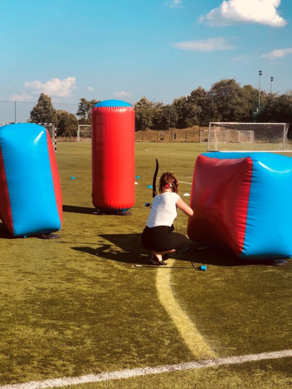 a battlezone archery, player, with bow and arrow ready to fire hiding behind the inflatable obstacles.