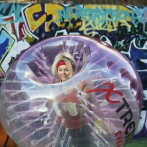 A pretty blonde female in a bubble football, with a graffiti backdrop.