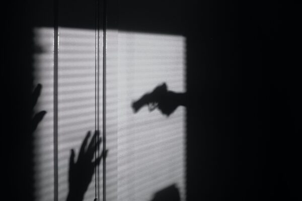 a black scene with white light projected onto the wall. there is a shadow of a gun and two hands being held up in surrender.