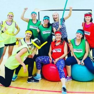 A group of ladies, dress for an old school sports day sitting on space hoppers. All smiles and cheering.