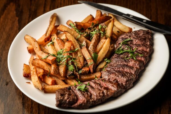 A white plate, with a succulent steak and fried chips.