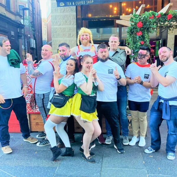 a group of men outside the Mayfair pub and kitchen in Newcastle. all with matching white t shirts, the say is dressed as a cheerleader and the 2 ladies in the picture in bavarian costumes.